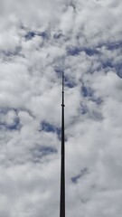 Obraz premium A towering lightning rod pierces a dramatic, cloudy sky streaked with deep blue. A minimalist, vertical shot from a low angle shows the contrast between the man-made structure and nature.