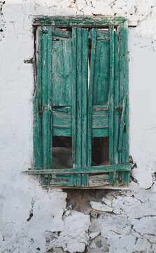 Weathered green and turquoise shutters on a crumbling whitewashed wall in Milos, Greece &mdash; a glimpse of Cycladic architecture and island heritage. Age and texture tell about Mediterranean lifestyle.