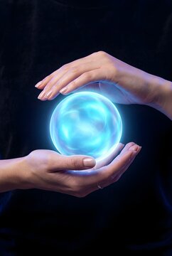Glowing blue crystal ball held between human hands on black background