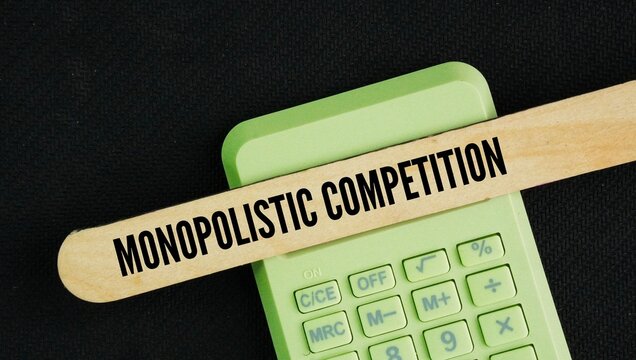 Calculator and wooden stick with the word monopolistic competition. market structure where many businesses sell products that are similar but not identical.