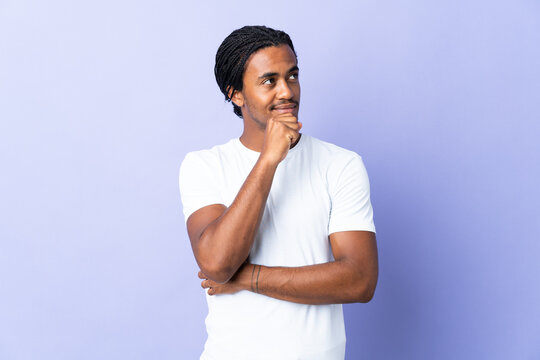 Young African American man with braids man isolated on purple background and looking up