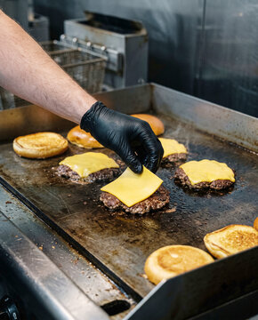 Chef in Black Glove Placing Cheese Slice on Burger Patty on Griddle