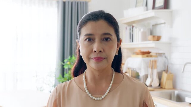 Smiling confident stylish Asian mature senior aged woman standing at home kitchen. Looking at camera arms crossed