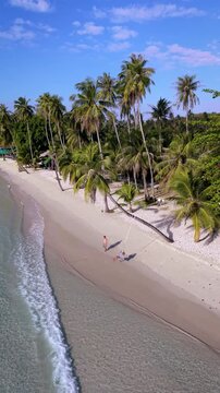 Relax on the pristine shores of Koh Kood Thailand, where soft sands meet crystal-clear waters. A couple enjoys tranquil moments surrounded by palm trees and vibrant nature in this tropical paradise.