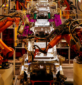 Automated robotic arms are welding at an automobile production plant.