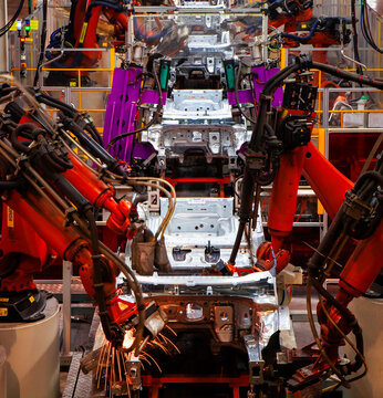 Automated robotic arms are welding at an automobile production plant.