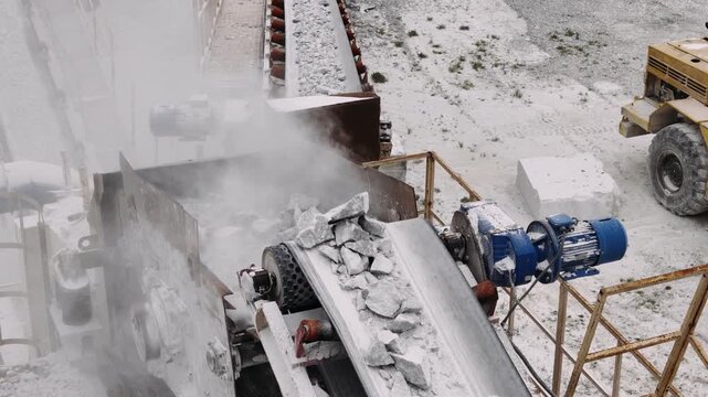 Industrial stone crusher crushing marble blocks on a conveyor belt. Heavy equipment processing raw materials at a manufacturing plant in a quarry