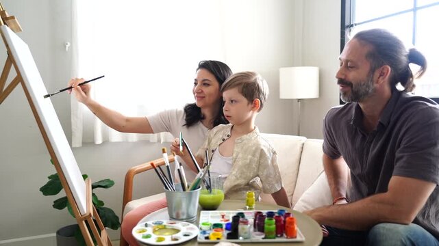 The family&mdash;mother, father, and son&mdash;are learning to paint with watercolors. The mother is teaching, the parents are teaching their son, and they are chatting as a hobby in the living room at home.