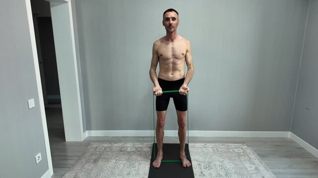 Muscular shirtless man exercising biceps with resistance band at home