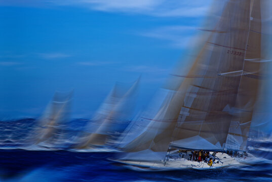 Luxury yachts racing on rough blue ocean water with crew on deck in fast action. Vintage 35mm film scan of sailboat regatta, motion blur, abstract sport background.