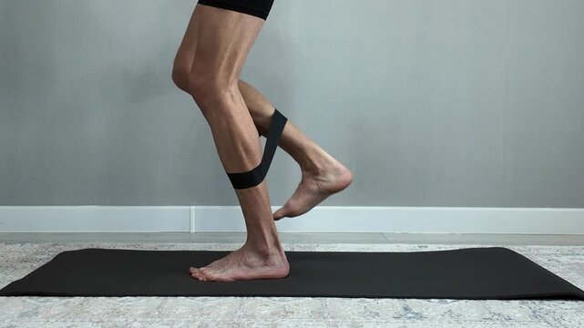 Muscular man performing leg extension exercises with a resistance band. Home workout for strengthening glutes, hamstrings, and calves