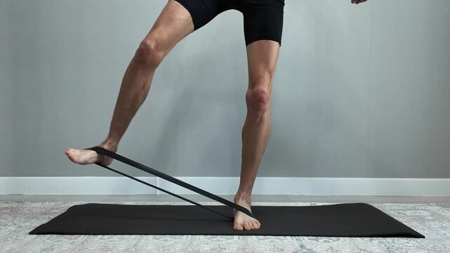 Athletic man's lower body strengthening the posterior tibialis tendon using a resistance band. Physical therapy exercise for foot and ankle stability