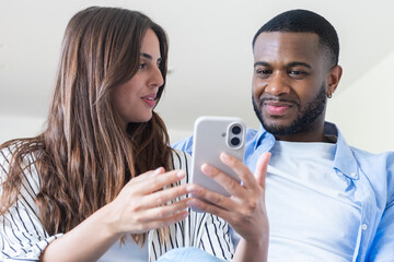 Fototapeta premium Young couple looking at smartphone together at home, smiling and sharing a moment of connection, technology, relationship and casual lifestyle