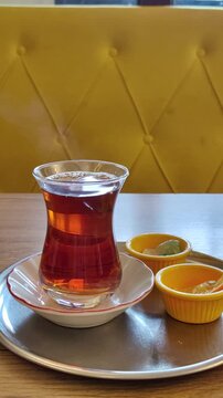 A traditional hot Turkish tea in an armudu  glass sits on a tray against the backdrop of a yellow sofa. A concept of Eastern hospitality, tea culture, and cozy relaxation.
