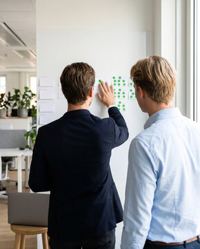Manager adding completed task marker to whiteboard during workplace accountability meeting