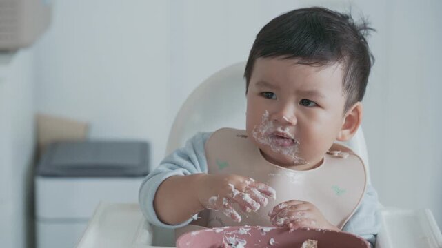Adorable toddler wearing a bib and enjoying self-feeding during baby-led weaning BLW.
