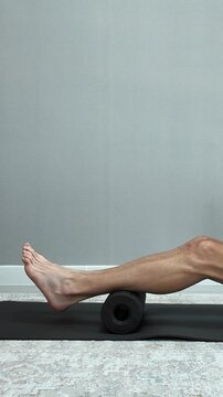 Athletic man massaging his hamstrings and calf muscles on a foam roller. Self-myofascial release for workout recovery at home