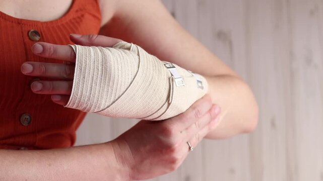 Woman with elastic compression bandage on wrist and palm. Medical care for joint pain, sports injuries or arthritis. Female hand with elastic bandage on wrist, close-up. Hand in medical bandage