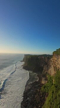 Vertical video. Smooth Aerial Flight Along Karang Boma Cliff At Sunset In Bali, Wide Angle View Of Towering Coastal Cliffs Above Ocean Waves And Golden Horizon, Freedom And Exploration