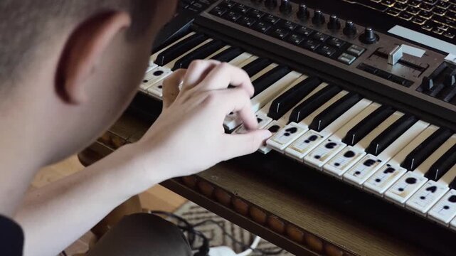 Young musician playing MIDI synthesizer keyboard with note stickers in home studio