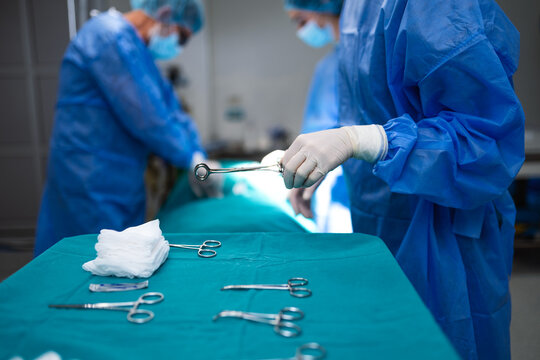 Close-up of surgical instruments on sterile table in operating room. Surgeon hand holding tool, blurry medical team performing operation in background. Concept of healthcare, surgery and medical.