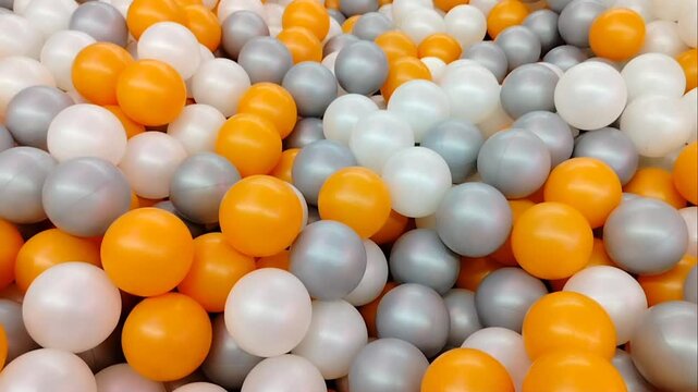 Colorful plastic balls background in ball pit with orange, white, and silver gray colors for playground or game area.