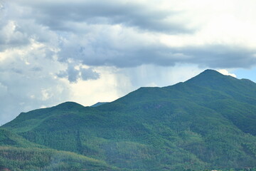 Obraz premium A scenic landscape view of rolling hills and mountain ridges covered with thick green forests under a dramatic overcast sky. Perfect for environment conservation blogs, hiking and adventure marketing,