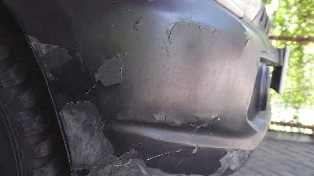 Close up of a damaged car front bumper with peeling and cracking paint texture, old grey automobile body requiring repair and professional respray.