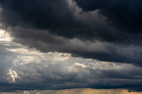 Ominous dark storm clouds accumulating before heavy rain at summer. Dramatic sky background covered with heavy dark storm clouds and lighter contrasting layers before powerful tempest