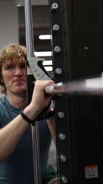 Vertical screen athlete performs deep squat on smith machine building leg strength stability and endurance with controlled movement during intense gym workout
