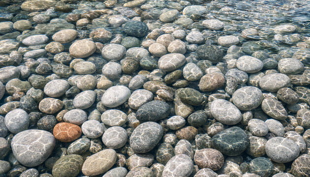 A collection of smooth, rounded river pebbles submerged in clear shallow water, showing light refraction patterns on the stone surfaces