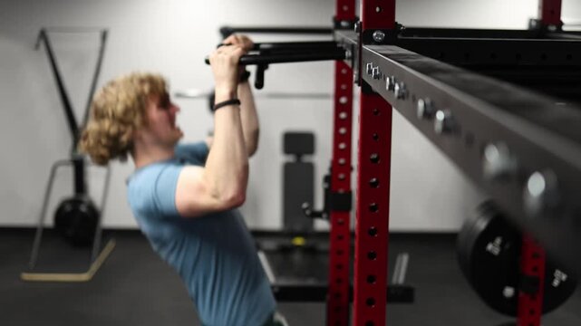 Young athlete performs strict pull up on horizontal bar building upper body strength grip power and endurance during focused calisthenics workout in modern gym
