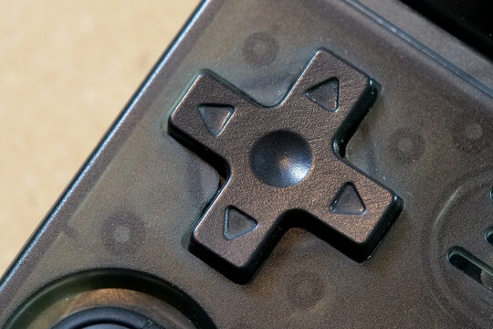 Classic black directional D-pad with four arrow buttons on a retro handheld gaming console, extreme close-up of generic video game controller hardware and navigation input, no people visible