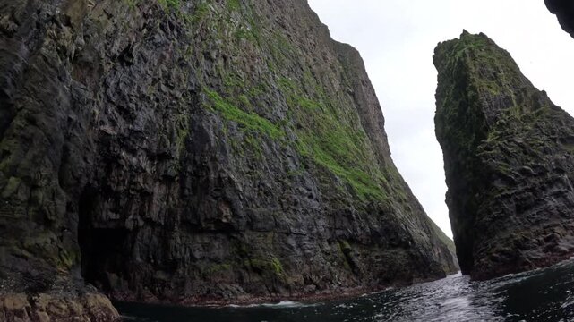 Boat POV sailing past a huge sea cave and towering basalt cliffs, Faroe Islands