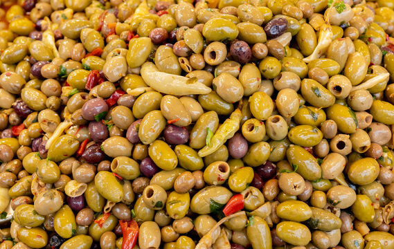 Large colorful assortment of marinated green and purple olives mixed with chili peppers, garlic and herbs at a farmers market, full-frame food background, close-up with no people