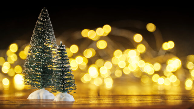 Christmas or New Year greeting card template with snow covered miniature Christmas trees and Christmas lights in the background. Xmas holidays atmosphere. Image with copy space and selective focus.	