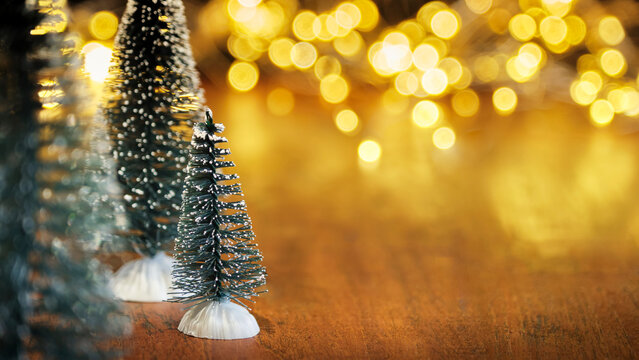 Christmas or New Year greeting card template with snow covered miniature Christmas trees and Christmas lights in the background. Xmas holidays atmosphere. Image with copy space and selective focus.