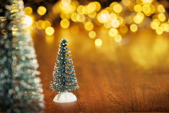 Christmas or New Year greeting card template with snow covered miniature Christmas trees and Christmas lights in the background. Xmas holidays atmosphere. Image with copy space and selective focus.