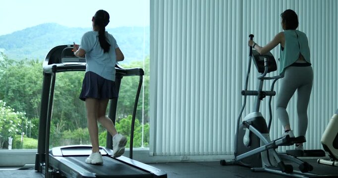 Two women working out on treadmill and elliptical machine with mountain view