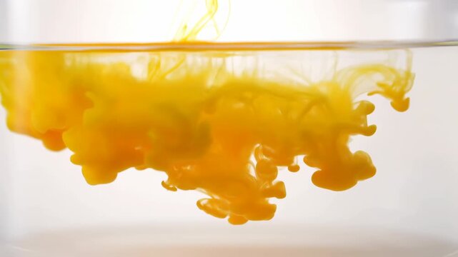 Yellow pigment pouring into clear water forming cloudlike submerged canopy with tendrils