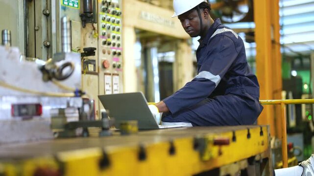 Industrial technician checking machine settings, laptop review, equipment inspection, manufacturing workflow, production monitoring, factory engineering, machine operation.