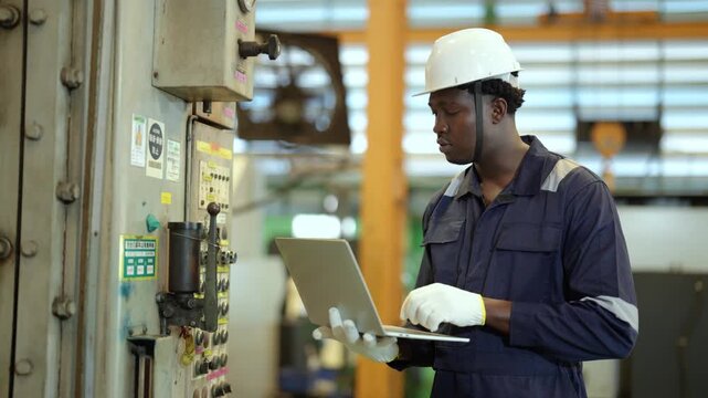 Factory technician operating industrial control panel, laptop monitoring, machine inspection, manufacturing process, production control, factory automation, industrial maintenance.