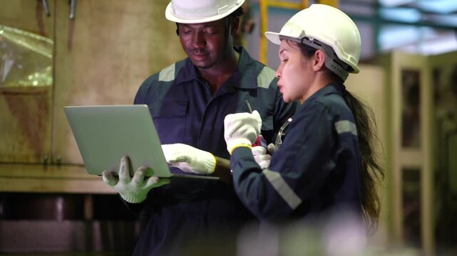 Male and female engineers discussing production process while walking in factory, laptop, walkie talkie, manufacturing teamwork, industrial operation, engineering collaboration.