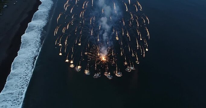 Aerial view of bright fireworks exploding over dark ocean water at night