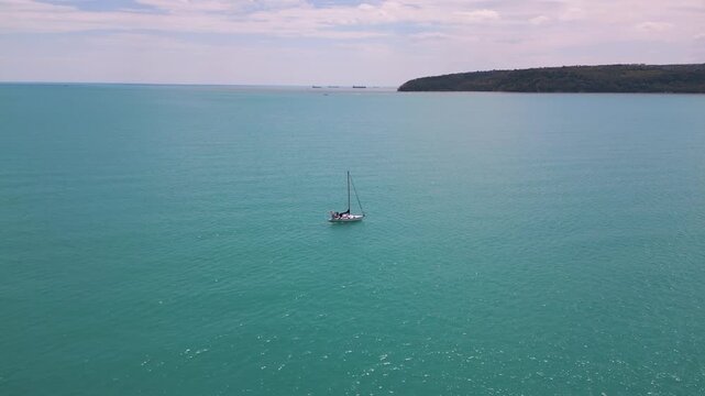 Aerial view of sailboat in turquoise sea near green coastline