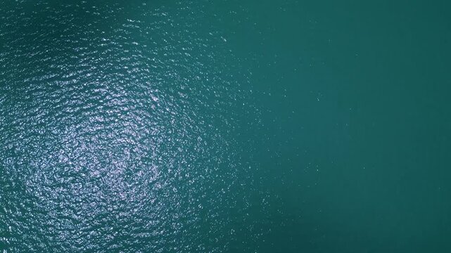 Aerial top down view of turquoise sea water surface with sun glares