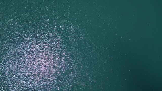 Aerial top down view of turquoise sea water surface with sun glares