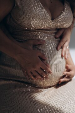 Close-up view of couple hands hugging pregnant woman belly in sequin dress