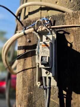 Indonesia - April 26, 2026 : Closeup view of electrical MCB from MERLIN GERIN ELECTRIC brand on pole with blurred background. Industrial photography concept design. Sunlight and shadow at hot day.