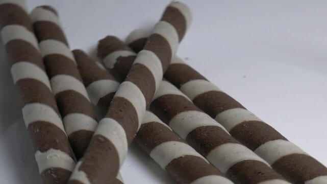 Close-up of striped chocolate wafer rolls rotating on a white plate, showcasing their spiral pattern and crispy texture under studio lighting.